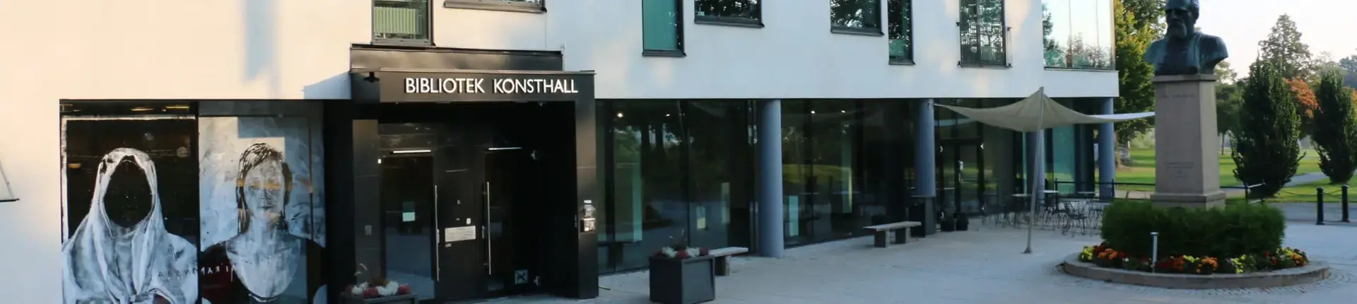 Fasad och byggnad i vitt med fönster, entré samt en byst vid sidan av.