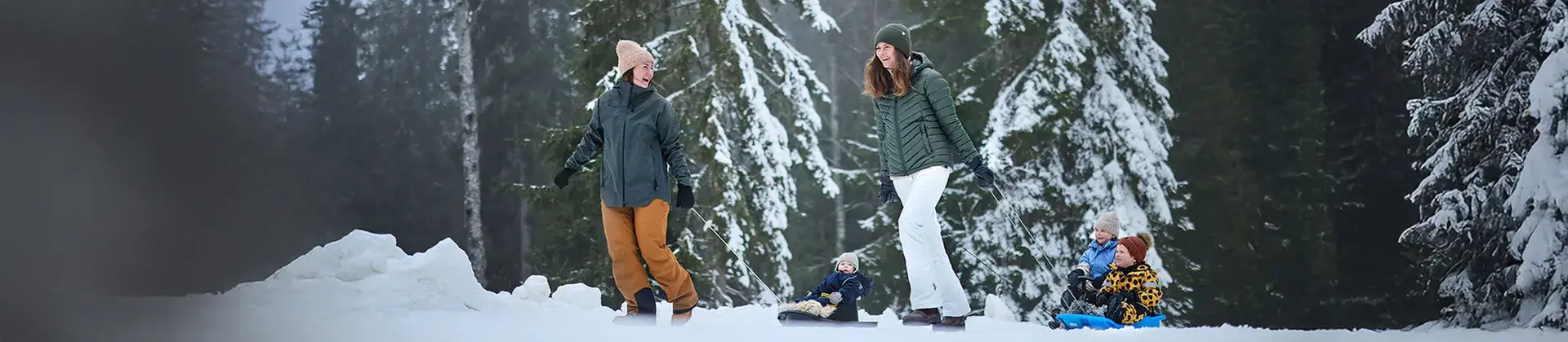 Två kvinnor drar ett par barn på pulka efter sig.