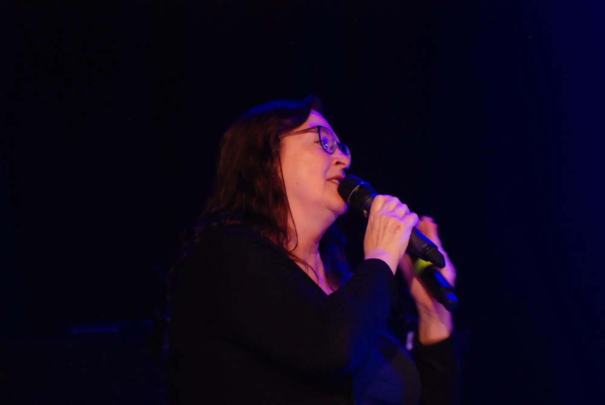 En leende kvinna med mörkt hår och glasögon står och pratar i en mikrofon.