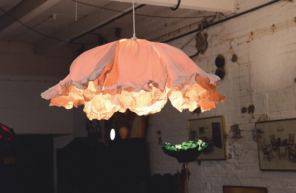 En lampa i rosa kräppapper som hänger i butiken. Den är tillverkad av Magdalena.