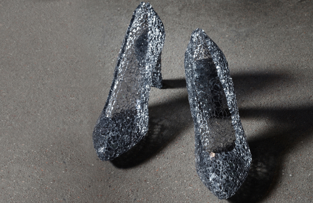 Ett par högklackade skor av glas på grå asfalt.